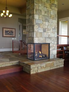 a fire place in the middle of a living room with wood flooring and stairs