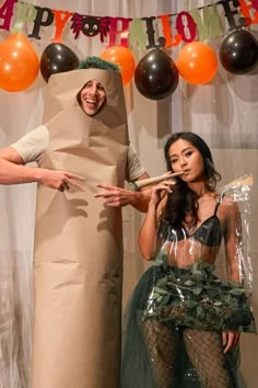 two people in costumes standing next to each other with balloons on the wall behind them