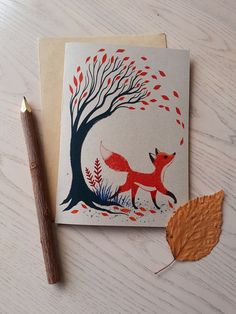 a card with an image of a fox under a tree and a pencil on the table