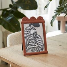 a wooden table topped with an orange and white frame next to a potted plant