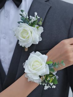 two white roses and greenery are on the arm of a man in a tuxedo