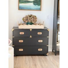 a black dresser with gold handles and drawers in front of a painting on the wall