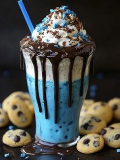 an ice cream sundae with chocolate chips and blue icing on the table next to cookies