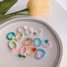 a white plate topped with lots of colorful bracelets next to a yellow tulip