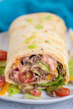 a burrito on a plate with lettuce, tomatoes and other toppings