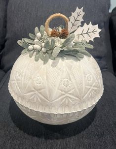 a white vase sitting on top of a black couch next to a wooden basket filled with leaves and acorns