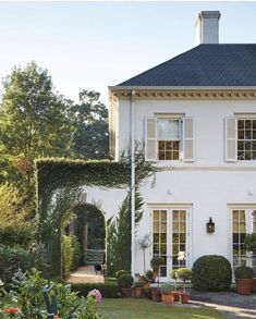 a white house with lots of potted plants in the front yard and an archway leading to it