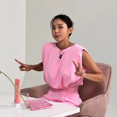 a woman in a pink dress sitting at a white table with a flower on it