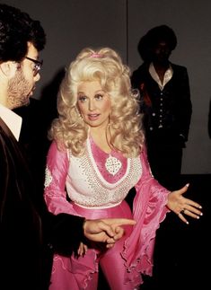 a man in a suit talking to a woman in a pink dress and white shirt