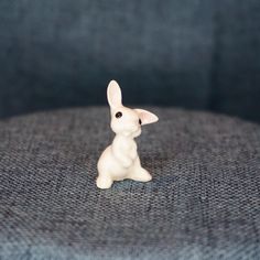 a small white rabbit figurine sitting on top of a blue couch cushion in front of the camera