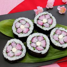 four sushi rolls on a plate with pink and white flowers in the background, ready to be eaten