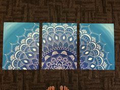 the feet are standing in front of three pieces of artwork on carpeted flooring