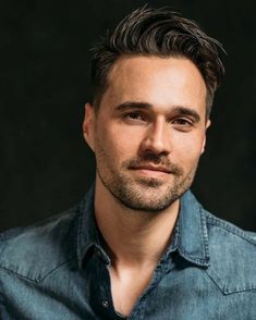 a close up of a person wearing a denim shirt and looking at the camera with a serious look on his face