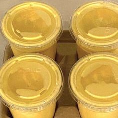 six yellow plastic cups sitting in a cardboard box with lids on each cup are shown