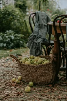 a wicker basket full of apples sitting on the ground next to a table and chairs