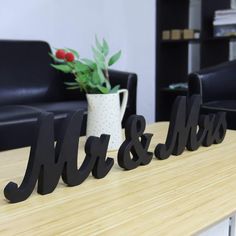 two black mr and mrs letters sitting on top of a wooden table next to a potted plant