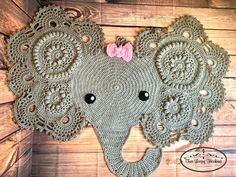 crocheted elephant head with pink bow on wooden wall