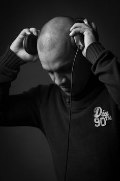 a bald man listening to headphones while wearing a black sweater and holding his hands on his ears