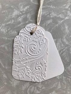 a white ceramic ornament hanging from a string on a gray tablecloth with leaves and snowflakes