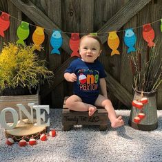 a baby sitting on top of a wooden box next to some plants and decorations in front of a fence