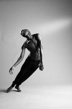 a shirtless man is dancing in the middle of an empty room with light coming from behind him