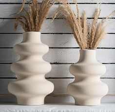 two white vases with dried grass in them