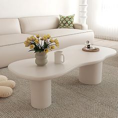 a living room with a white couch, coffee table and flowers in a vase on the floor