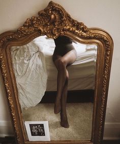 a woman's legs are visible in the reflection of a gold framed mirror,