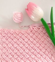 a pink knitted blanket with two tulips on top and a crochet hook