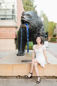 a woman sitting in front of a statue of a bear with a blue ribbon around its neck