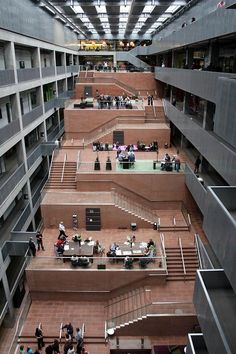 an indoor tennis court with stairs and people on the other side, surrounded by buildings