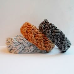 three crocheted objects are sitting on a white surface, one is gray and the other is orange