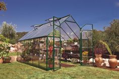 a green house in the middle of a garden with potted plants and other flowers