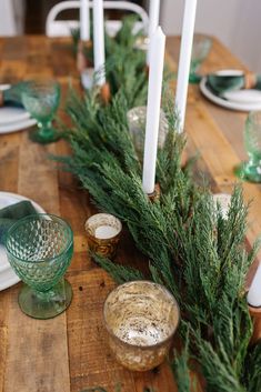 a wooden table topped with candles and dishes covered in greenery on top of it