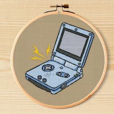 a cross stitch picture of an old nintendo gameboy on a wooden surface with the screen partially closed