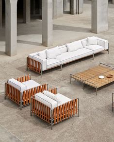 an outdoor seating area with white couches and wooden tables on cement ground next to concrete pillars