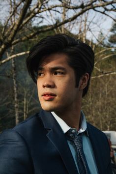 a young man in a suit and tie looking off into the distance with trees in the background