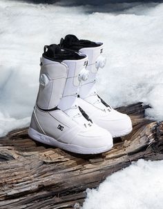 a pair of white snowboard boots sitting on top of a log in the snow