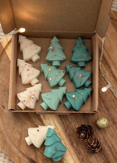 a box filled with blue and white decorated cookies next to a pine cone on top of a wooden table