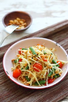 a white bowl filled with pasta and vegetables on top of a place mat next to a fork