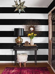 a room with black and white stripes on the walls, a table with flowers in vases and a star shaped mirror above it