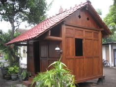 a small wooden building with a red roof and some potted plants in front of it