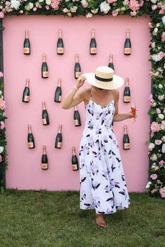 a woman standing in front of a pink wall with lots of wine bottles on it