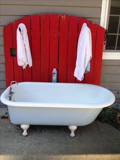 a white bath tub sitting in front of a red wall with towels hanging on it