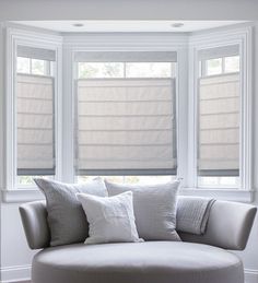 a round couch sitting in front of two windows with roman shades on the windowsill