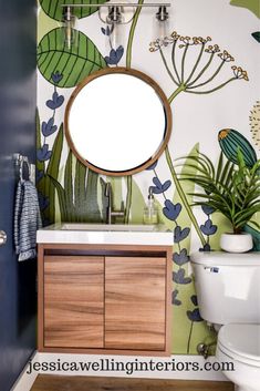 a bathroom with green and blue wallpaper, white toilet and wooden vanity sink cabinet