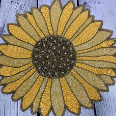 a yellow and brown beaded sunflower sitting on top of a wooden table