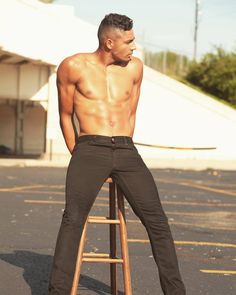 a shirtless man sitting on top of a wooden stool