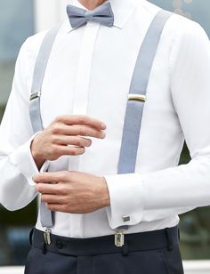 a man wearing a white shirt and blue suspenders is holding his hands in his pocket