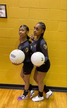 two girls in uniforms holding volleyballs and posing for the camera